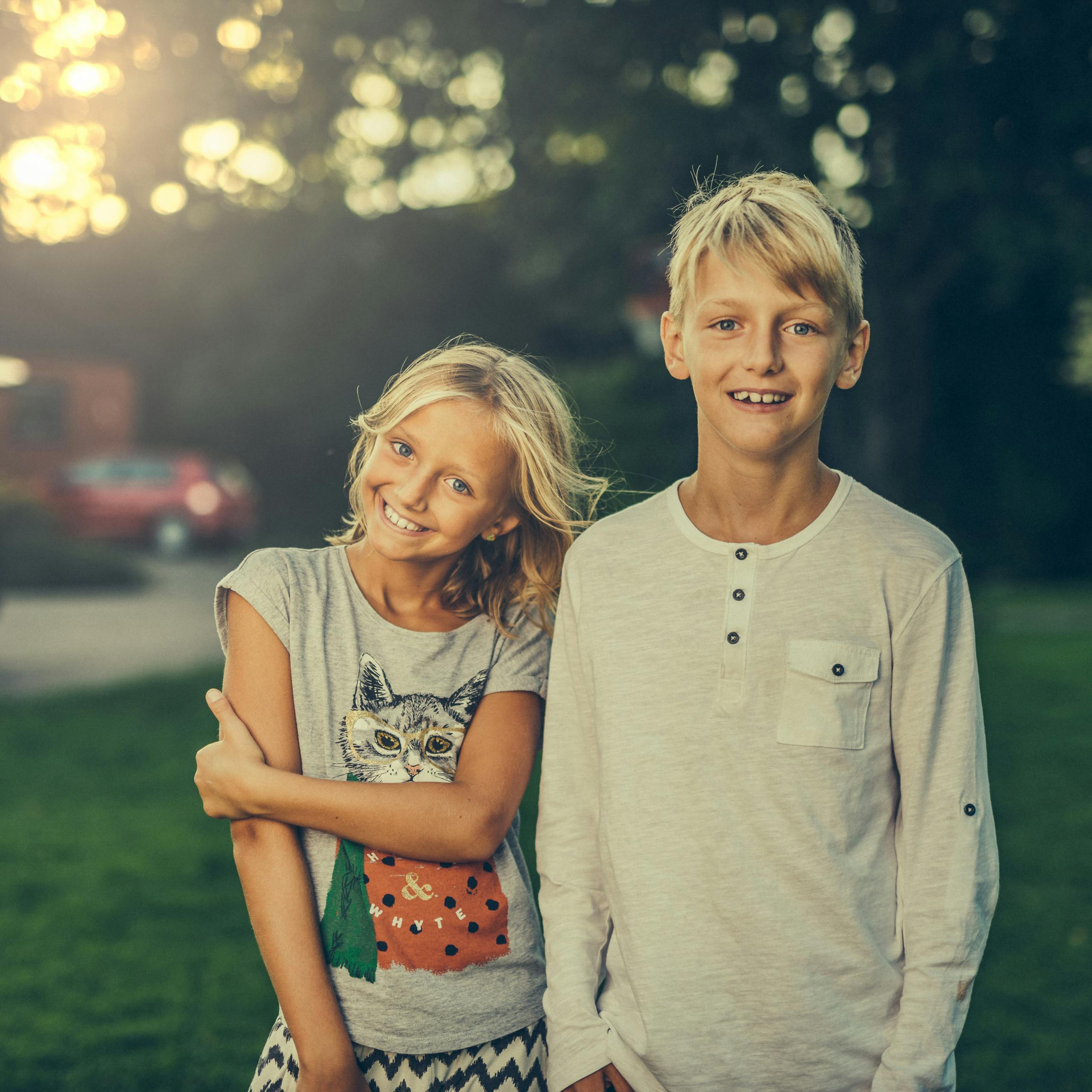 A joyful brother and sister smiling outdoors in a sunlit garden. Perfect stock photo for family and lifestyle themes.